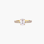 Gold-plated solitaire ring with oval zirconia center stone and pavé band on cream background