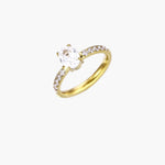 Gold-plated solitaire ring with oval zirconia center stone and pavé band on cream background