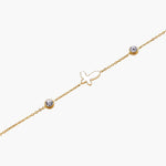 Gold chain bracelet with white mother of pearl butterfly pendant and two bezel-set crystals on cream background