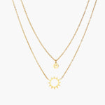 Gold layered necklace set with sunburst and smiley face pendants on delicate chains against white background.