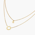 Gold layered necklace set with sunburst and smiley face pendants on delicate chains against white background.