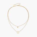 Gold layered necklace set with sunburst and smiley face pendants on delicate chains against white background.