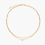 Delicate double-chain gold necklace with tiny heart pendant on cream background
