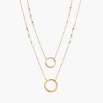 Layered gold necklace set with two open circle pendants and mixed chain styles on beige background