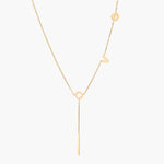 Gold Y-shaped necklace with L-O-V-E letter charms and vertical bar pendant on delicate chain against cream background