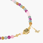 Stretchable bracelet with pastel gemstone beads, freshwater pearls, gold centerpiece and butterfly charm on cream background